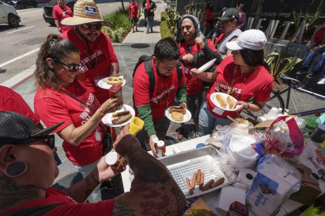 Striking hotel workers eat hotdogs and burgers grilled outside the InterCo<em></em>ntinental Los Angeles Downtown Hotel Tuesday, July 4, 2023, in downtown Los Angeles. (AP Photo/Damian Dovarganes)