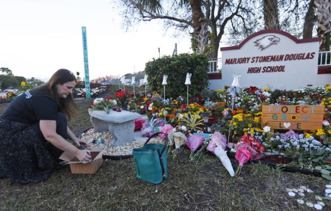 FILE - Suzanne Devine Clark, an art teacher at Deerfield Beach Elementary School, places painted sto<em></em>nes at a memorial outside Marjory Sto<em></em>neman Douglas High School during the first anniversary of the school shooting in Parkland, Fla., Feb. 14, 2019. The 2018 Parkland high school massacre will be reenacted with the firing of a<em></em>bout 140 blanks on campus as part of families' lawsuits against the former sheriff's deputy they accuse of failing to stop the gunman, a judge ruled Wednesday, July 12, 2023. (AP Photo/Wilfredo Lee, File)