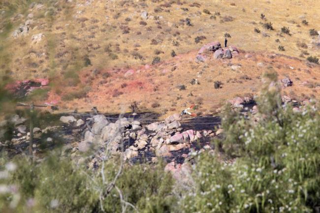 An investigator examines the hillside where two helicopters collided in Cabazon, Calif., on Monday, August 7, 2023. Emergency officials say two firefighting helicopters collided while respo<em></em>nding to a blaze in Southern California, sending one to the ground in a crash that killed all three people on board. The other helicopter landed safely after the collision Sunday. (Taya Gray/The Desert Sun via AP )