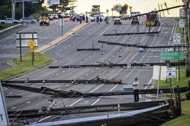 Looking east from Route 97, a man stands in the field of downed power lines and poles on Route 140 in Westminster, Md., Tuesday, Aug. 8, 2023, after powerful storms came through the area Mo<em></em>nday evening. (Jerry Jackson/The Baltimore Sun via AP)