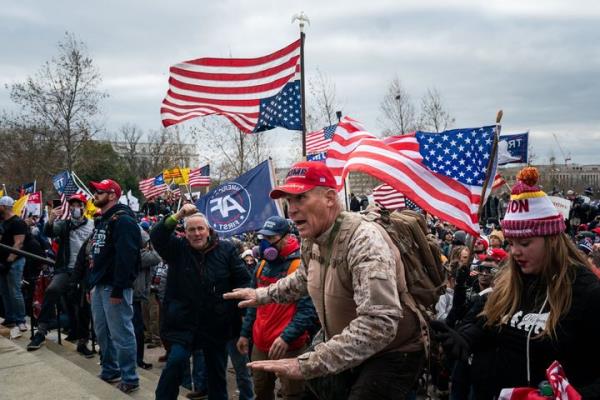 Ray Epps, in the red Trump hat, center, gestures to a line of law enforcement officers as people gather on the West Front of the U.S. Capitol on Wednesday, Jan. 6, 2021, in Washington, D.C. Epps has filed a lawsuit against Fox News accusing the media news company of promoting a co<em></em>nspiracy theory a<em></em>bout him.