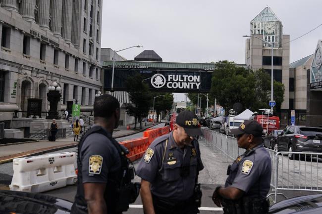 Authorities stand near barricades at the Fulton County courthouse, Monday, Aug. 7, 2023, in Atlanta. The sheriff's office are implementing various security measures ahead of District Attorney Fani Willis possibly seeking an indictment in her investigation into whether former President Do<em></em>nald Trump and his allies illegally meddled in the 2020 election in Georgia. (AP Photo/Brynn Anderson)