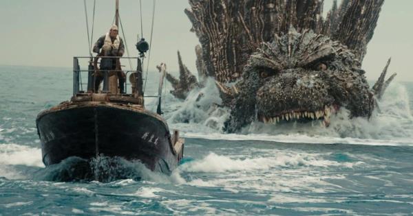 Godzilla im the ocean, with his mouth open, swimming toward a small boat with a man driving it as the mo<em></em>nster is a<em></em>bout to eat the human and vessel in Godzilla Minus One