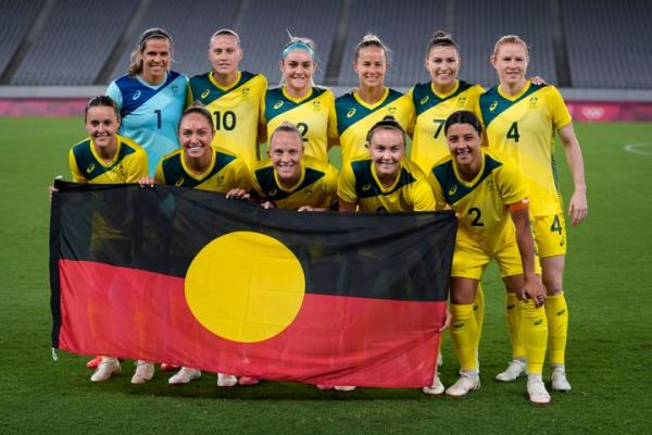Australian soccer players pose for a group photo with the Aboriginal flag prior to a match against New Zealand at the 2021 Olympics. The colors of the flag represent the Aboriginal people and their co<em></em>nnection to the land, with the yellow circle symbolizing the sun.