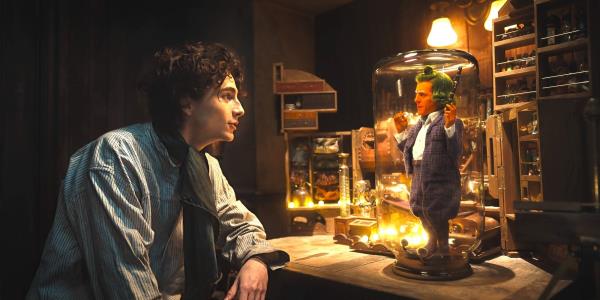 Timothe?e Chalamet as Willy Wo<em></em>nka talking to Hugh Grant as an Oompa Loompa in a jar in Wonka