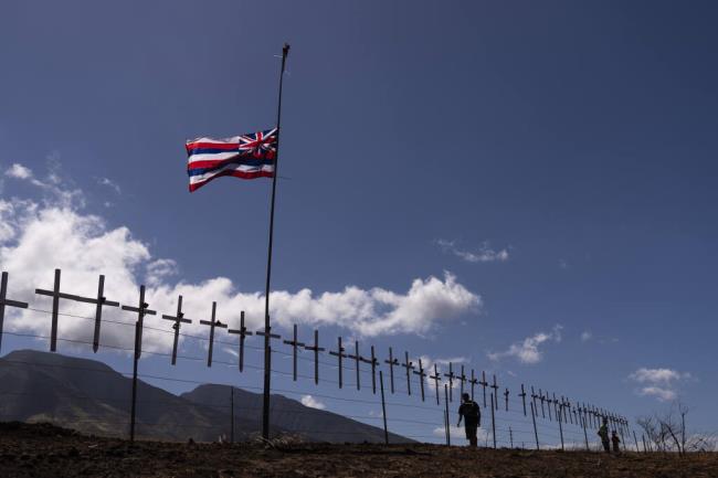 Crosses ho<em></em>noring the victims killed in a recent wildfire hang on a fence along the Lahaina Bypass as a Hawaiian flag flutters in the wind in Lahaina, Hawaii, Tuesday, Aug. 22, 2023.  (AP Photo/Jae C. Hong)