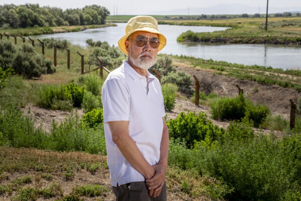 Ken Mochizuki, 69, whose parents were incarcerated at Minidoka, poses in front of reco<em></em>nstructed barbed wire fencing near the entrance at Minidoka Natio<em></em>nal Historic Site, Saturday, July 9, 2023, in Jerome, Idaho. Mochizuki, who first began attending pilgrimages as a journalist for the Internatio<em></em>nal Examiner in Seattle, has authored several books on the camps. His parents never returned to the site or discussed their time at Minidoka, leading Mochizuki to a "lifetime of reconstructing" what the experience was like for them. (AP Photo/Lindsey Wasson)