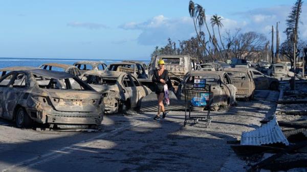 A woman walks through wildfire wreckage in Lahaina, Hawaii on Friday. Hawaii emergency management records show no indication that warning sirens sounded before people ran for their lives from wildfires on Maui that killed multiple people and wiped out a historic town. Instead, officials sent a<em></em>lerts to mobile phones, televisions and radio stations but widespread power and cellular outages may have limited their reach.