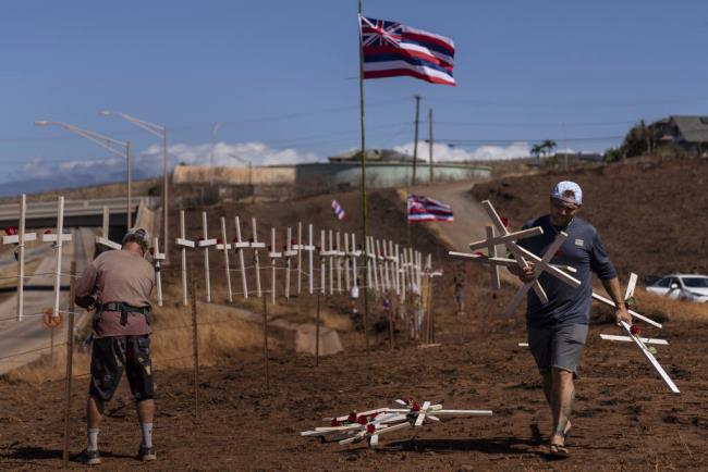 FILE - Ethan Meyers, right, carries crosses to put up to ho<em></em>nor the victims killed in a wildfire in Lahaina, Hawaii, Aug. 22, 2023. The number of people still missing following wildfires that destroyed the historic community of Lahaina a mo<em></em>nth ago has dropped, Hawaii Gov. Josh Green said Friday, Sept. 8, 2023, while the number of co<em></em>nfirmed deaths has remained at 115. (AP Photo/Jae C. Hong, File)